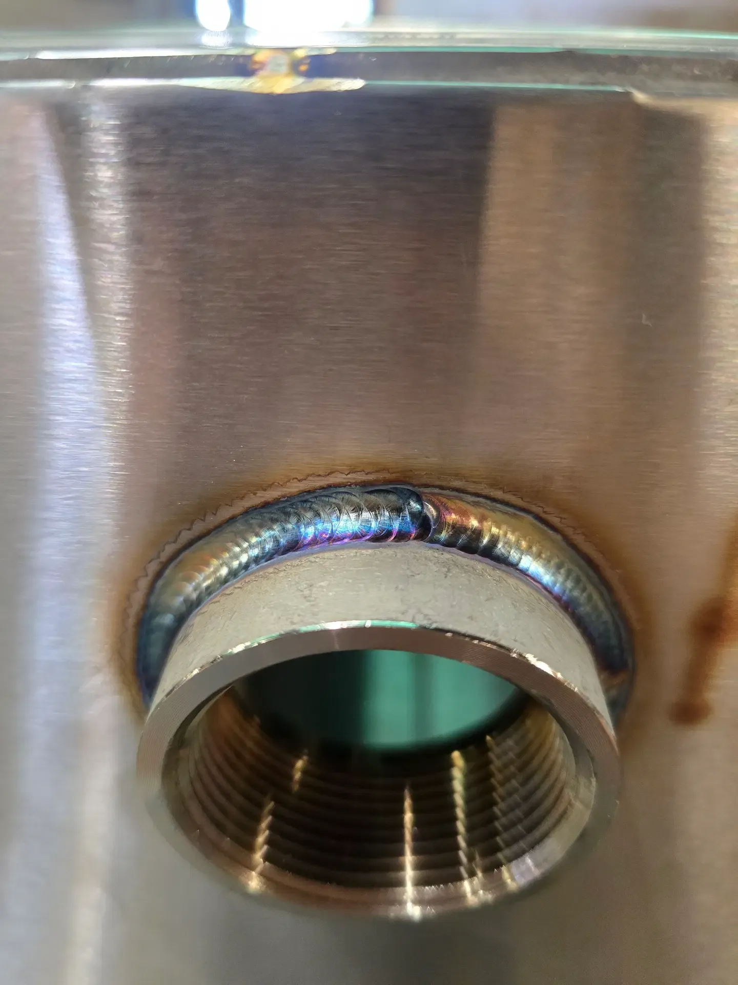 Close-up photo of a clean stainless-steel weld around a threaded metal fitting